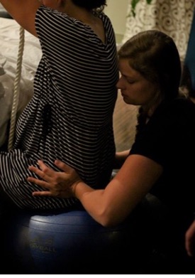 Woman in first stages of Labour sitting on Birthing Ball with her Doula giving Hip Squeezes